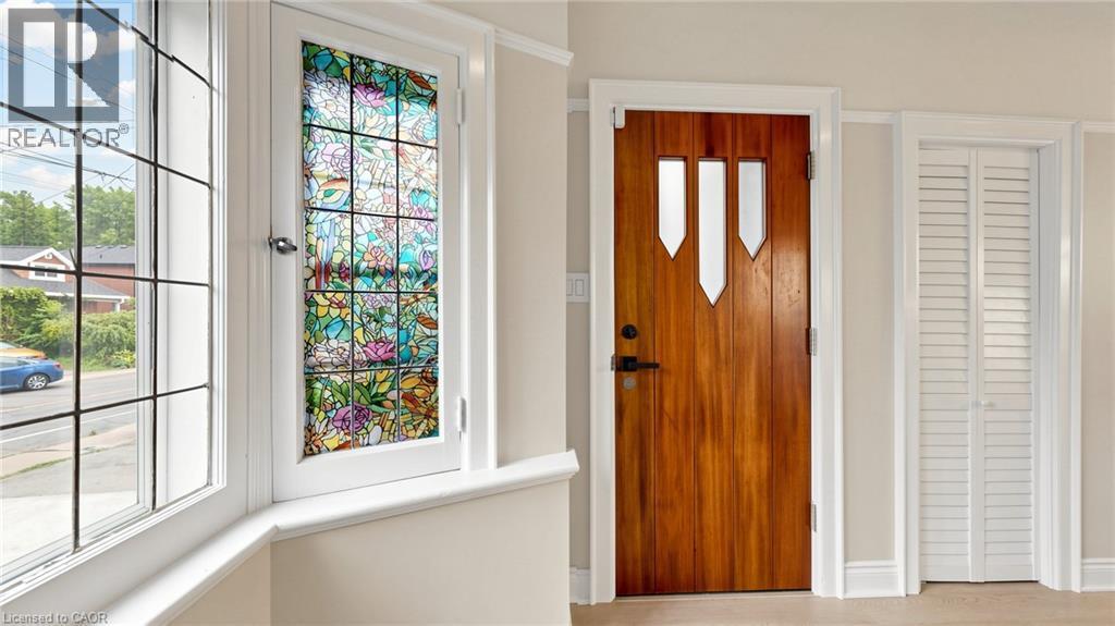 Hardwood entry door with decorative glass inserts, accompanied by a bay window featuring a stained-glass panel and grid-patterned panes - 59 Longwood Road N, Hamilton, ON - Indoor Photo Showing Other Room