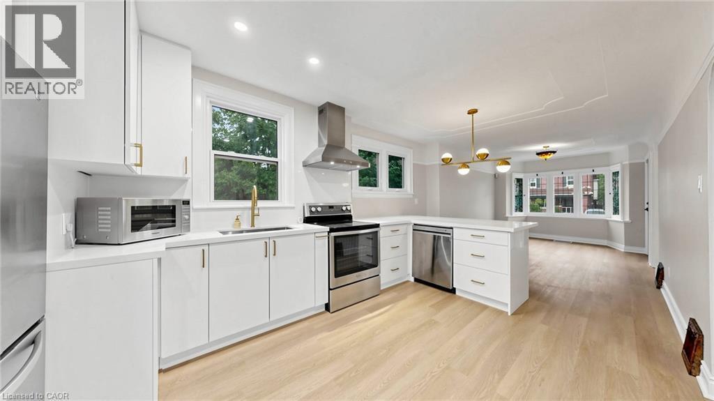 Open-concept kitchen featuring white cabinetry, stainless steel appliances, a center island, and wood-finish flooring - 59 Longwood Road N, Hamilton, ON - Indoor Photo Showing Kitchen With Stainless Steel Kitchen With Upgraded Kitchen
