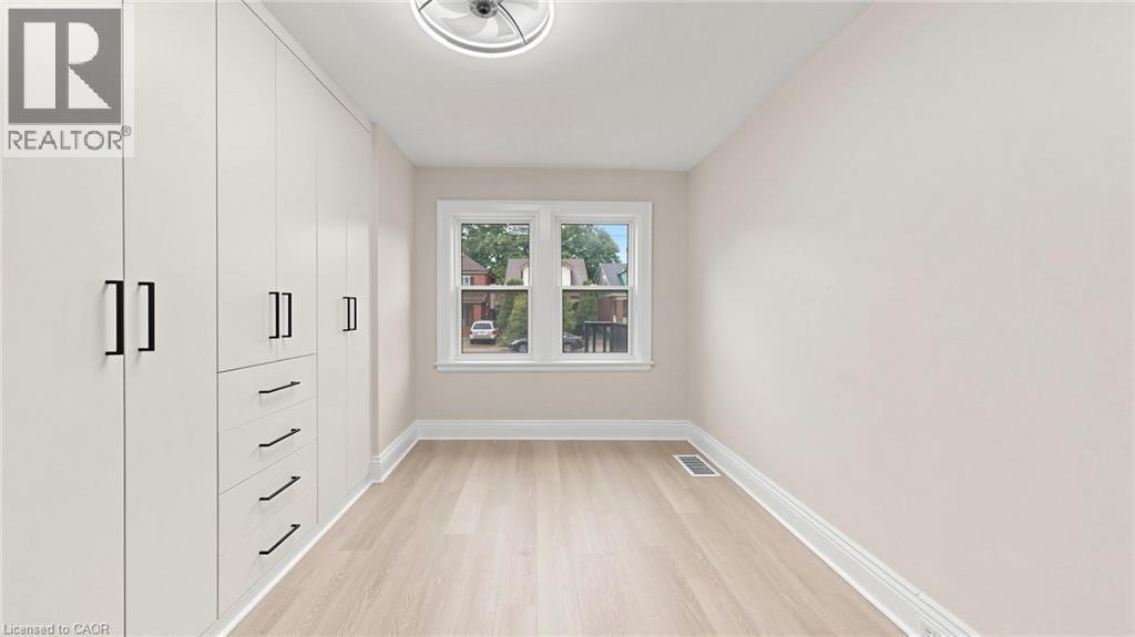 Spacious room featuring a wall of integrated cabinetry with matte black hardware, light wood-finish flooring, and a contemporary ceiling light fixture - 59 Longwood Road N, Hamilton, ON - Indoor Photo Showing Other Room