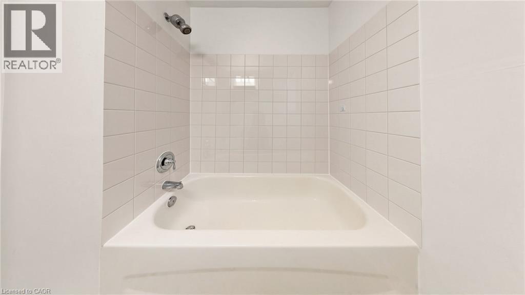White subway tile shower surround with integrated bathtub and chrome fixtures - 59 Longwood Road N, Hamilton, ON - Indoor Photo Showing Bathroom
