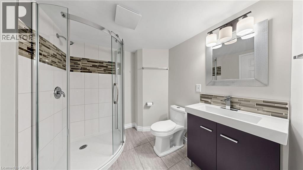 Bathroom featuring a curved glass shower enclosure, white subway tile with an accent mosaic band, a built-in vanity with a rectangular sink, a framed mirror, and a three-light vanity fixture - 59 Longwood Road N, Hamilton, ON - Indoor Photo Showing Bathroom