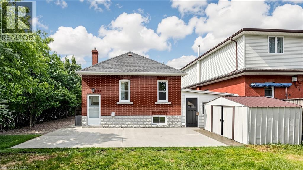 Brick exterior with a stone foundation accent, featuring a gray shingle roof and a concrete patio - 59 Longwood Road N, Hamilton, ON - Outdoor