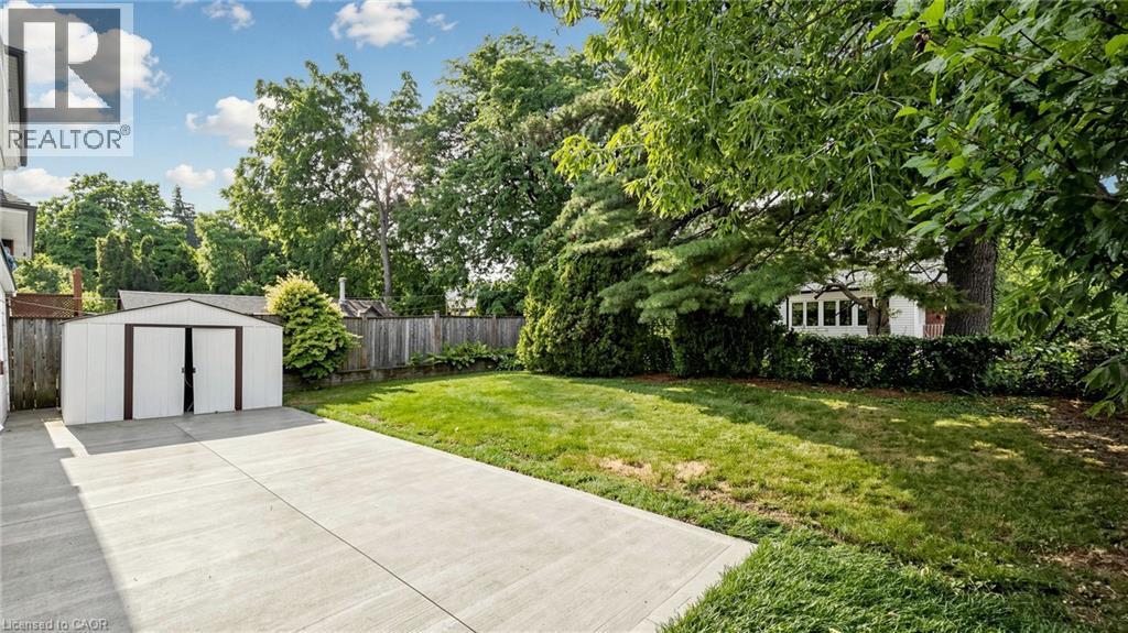 Expansive concrete patio with a detached storage shed, offering a manicured lawn and mature trees - 59 Longwood Road N, Hamilton, ON - Outdoor