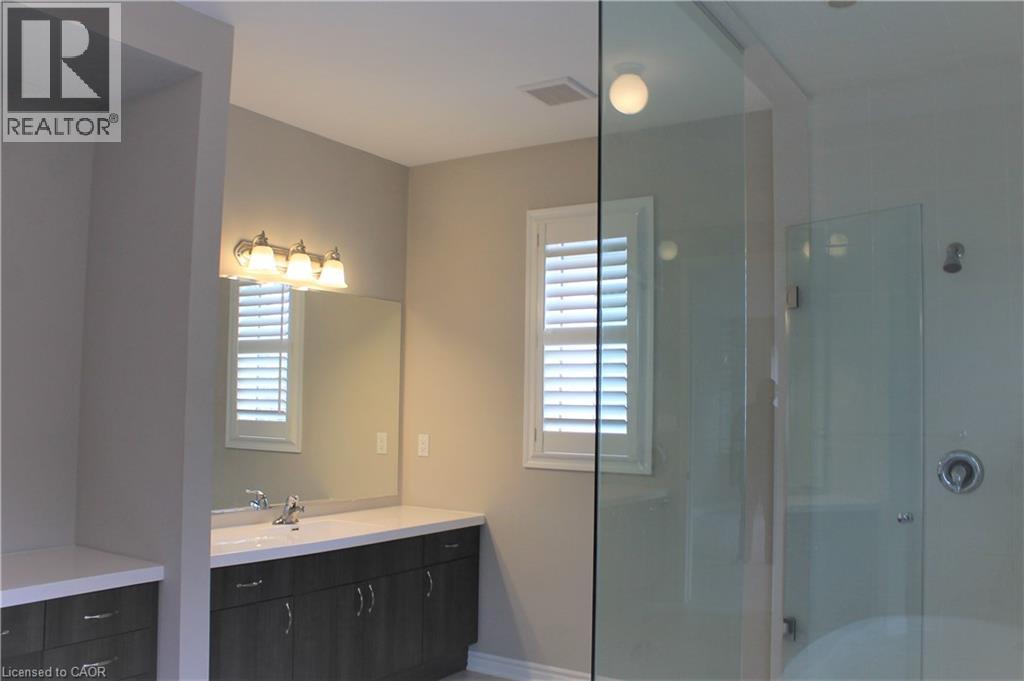 Bathroom featuring a glass-enclosed shower, a vanity with a white countertop and dark wood-finish cabinetry, a rectangular mirror, and a window with white plantation shutters - 31 Pointer Street Unit# Main Floor, Cambridge, ON - Indoor Photo Showing Bathroom