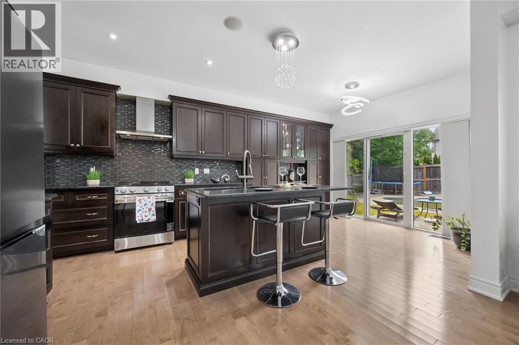 Gourmet kitchen featuring dark wood cabinetry, stainless steel appliances, a tile backsplash, and a central island with bar seating - 145 Redtail Street, Kitchener, ON - Indoor Photo Showing Kitchen With Upgraded Kitchen