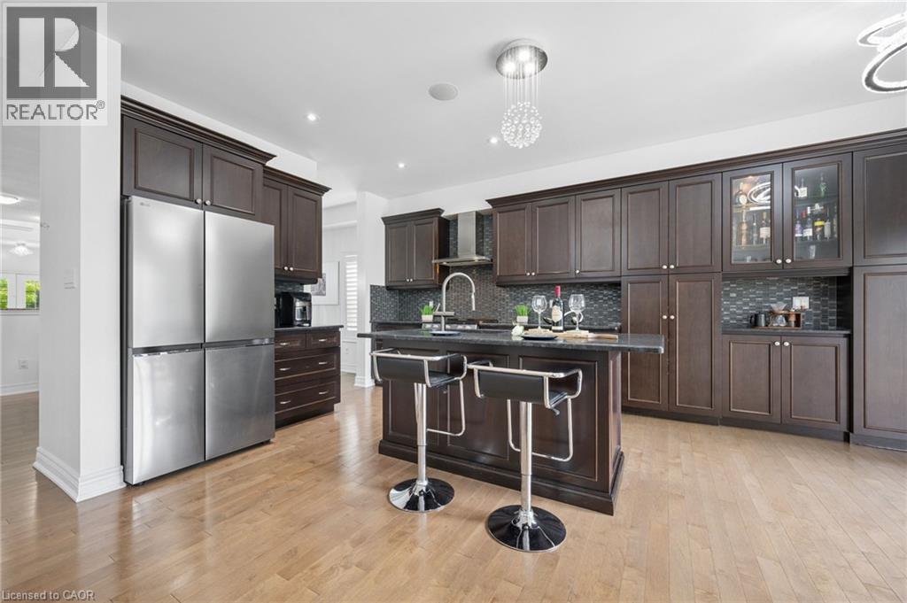 Kitchen featuring dark wood cabinetry, stainless steel appliances, a dark countertop island, a mosaic tile backsplash, and light wood-finish flooring - 145 Redtail Street, Kitchener, ON - Indoor Photo Showing Kitchen With Stainless Steel Kitchen With Upgraded Kitchen