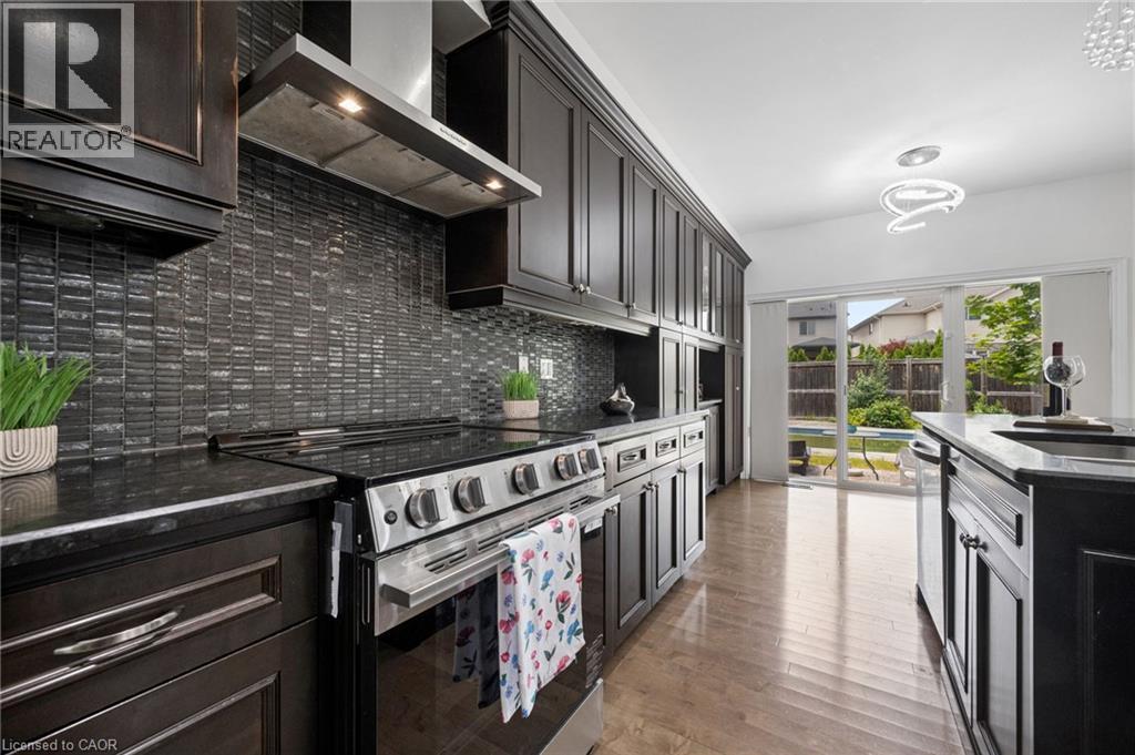 Kitchen featuring dark wood cabinetry, stainless steel appliances, dark stone countertops, and a full-height tile backsplash - 145 Redtail Street, Kitchener, ON - Indoor Photo Showing Kitchen With Upgraded Kitchen