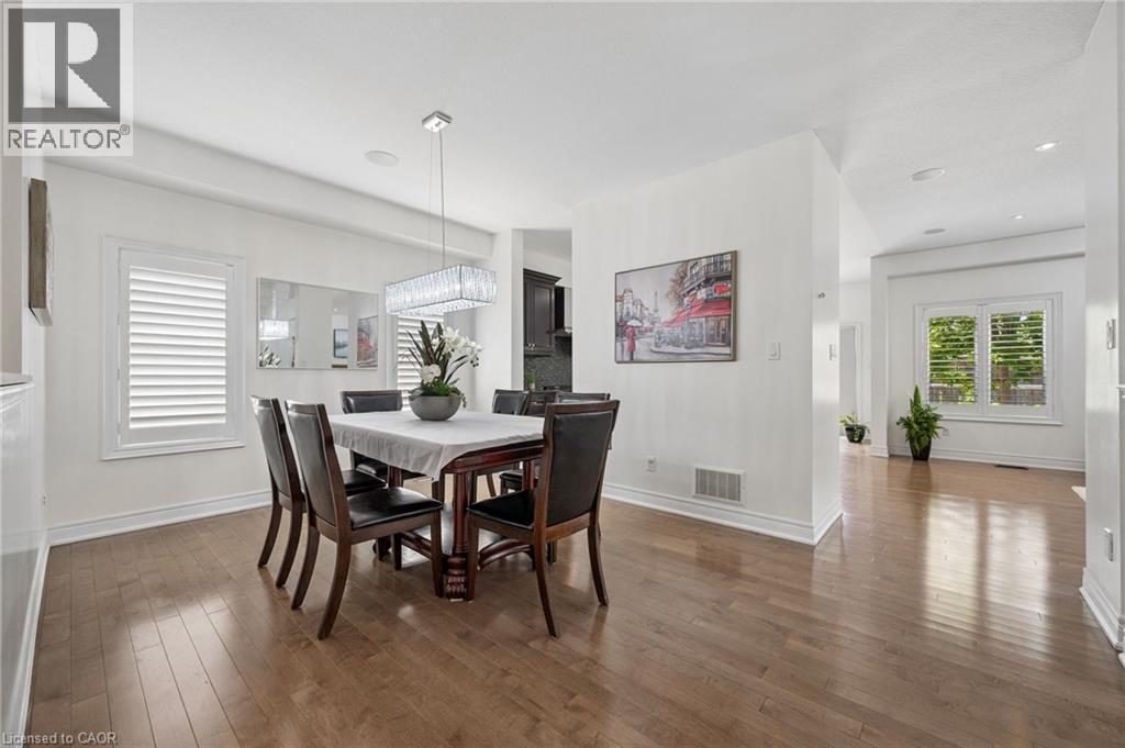 Dining area with wood-finish flooring, white plantation shutters, and a contemporary linear crystal chandelier - 145 Redtail Street, Kitchener, ON - Indoor Photo Showing Dining Room
