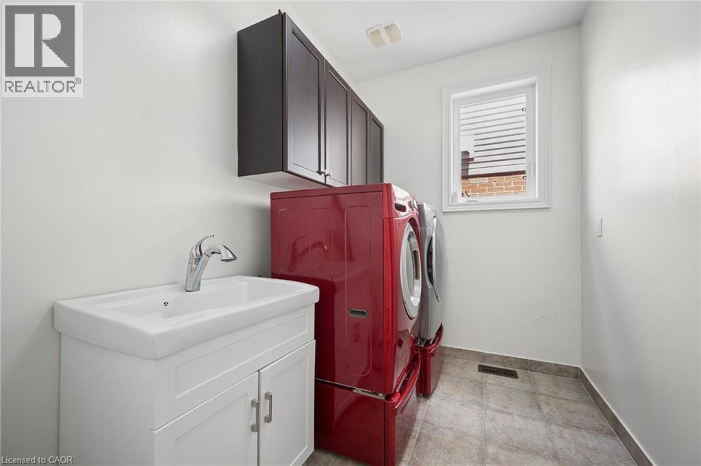 Laundry area featuring a single window, overhead cabinetry, a vanity with an integrated sink, and tiled flooring - 145 Redtail Street, Kitchener, ON - Indoor Photo Showing Laundry Room