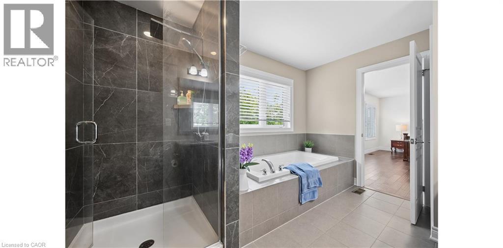 Spacious bathroom featuring a glass-enclosed shower with dark-toned tile surround, a built-in tub with light gray tile surround, and light tile flooring - 145 Redtail Street, Kitchener, ON - Indoor Photo Showing Bathroom