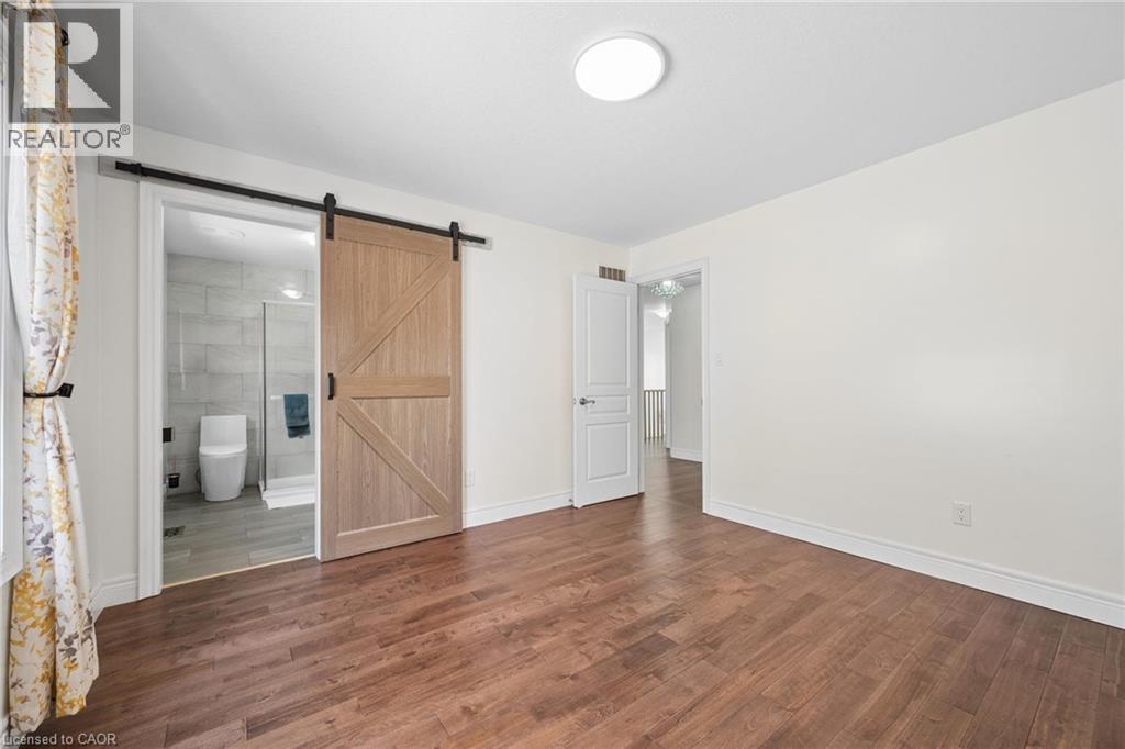 Spacious room featuring wood-finish flooring, white baseboards, and a modern ceiling light fixture - 145 Redtail Street, Kitchener, ON - Indoor