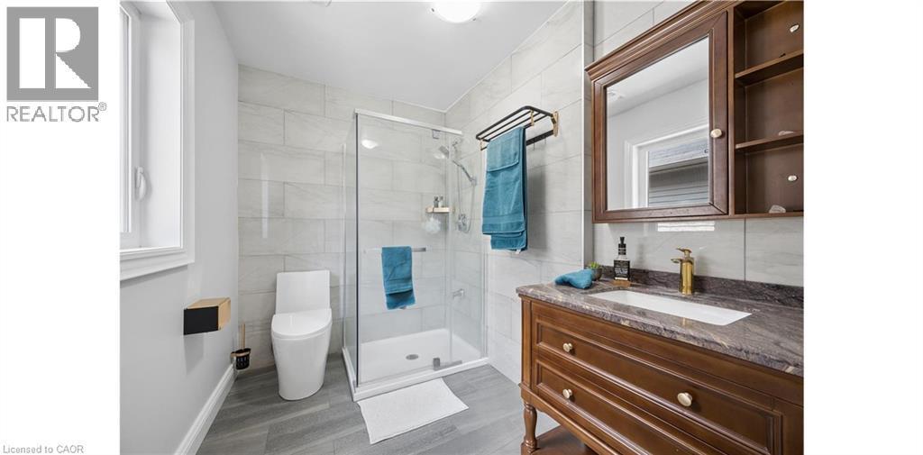 Contemporary bathroom featuring a glass-enclosed shower with tile surround, a modern toilet, wood-finish vanity with a stone countertop, an undermount sink, and a gold-finish faucet - 145 Redtail Street, Kitchener, ON - Indoor Photo Showing Bathroom