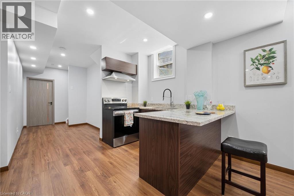 Contemporary kitchen featuring a stainless steel range, granite countertops, wood-finish flooring, recessed lighting, and a modern island with seating - 145 Redtail Street, Kitchener, ON - Indoor Photo Showing Kitchen
