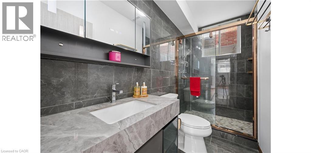 Bathroom featuring a floating vanity with an integrated sink, a large mirrored medicine cabinet, a walk-in shower with a glass enclosure, dark tile flooring, and dark tile walls - 145 Redtail Street, Kitchener, ON - Indoor Photo Showing Bathroom