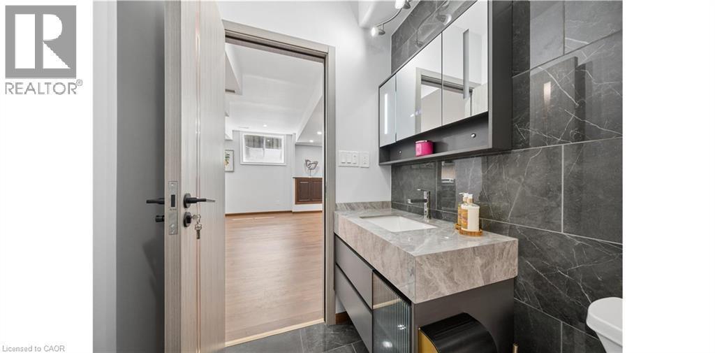 Bathroom featuring a built-in vanity with a stone countertop and integrated sink, a wall-mounted mirrored medicine cabinet, and large-format dark stone-look wall tiles - 145 Redtail Street, Kitchener, ON - Indoor Photo Showing Bathroom