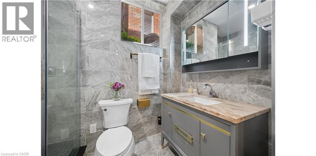 Bathroom featuring full-height marble-look tiling, a glass-enclosed shower, a vanity with a light-toned stone countertop, and an illuminated medicine cabinet - 145 Redtail Street, Kitchener, ON - Indoor Photo Showing Bathroom