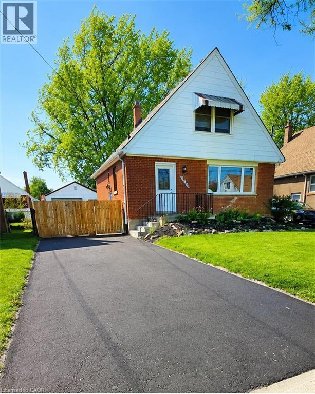 Brick and white siding exterior with a pitched roof, featuring a paved driveway, front lawn, and wooden fence - 274 East 38Th Street, Hamilton, ON - Outdoor