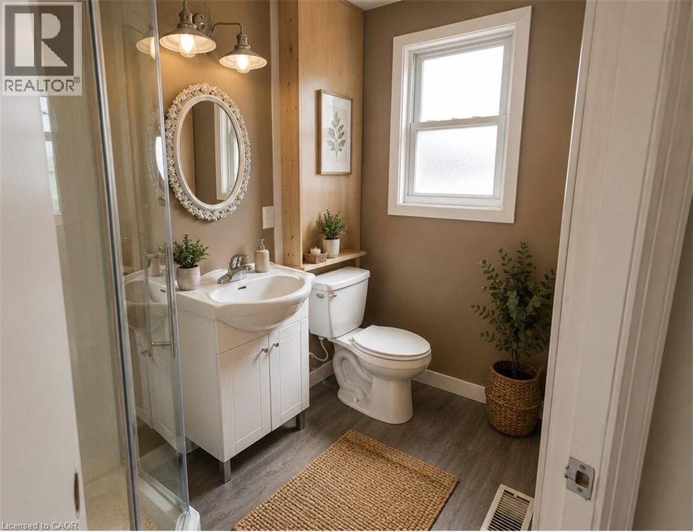 Bathroom featuring a white vanity with integrated sink, glass-enclosed shower, wood-finish flooring, and a window with white trim - 274 East 38Th Street, Hamilton, ON - Indoor Photo Showing Bathroom