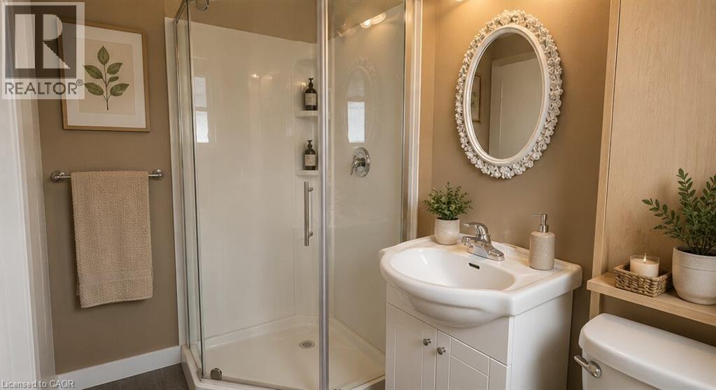 Bathroom featuring a glass-enclosed shower, white vanity with integrated sink, oval framed mirror, and a toilet with a wood-finish shelf above - 274 East 38Th Street, Hamilton, ON - Indoor Photo Showing Bathroom