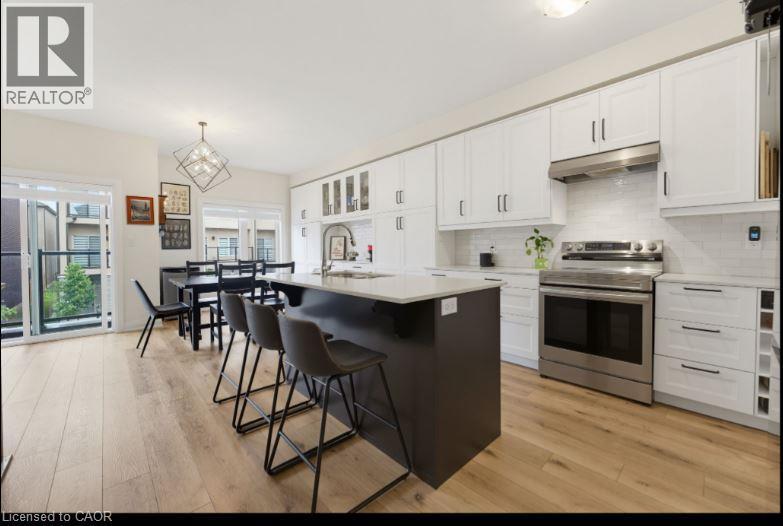 Kitchen featuring white upper and lower cabinetry, stainless steel appliances, a dark-toned island with seating, light wood-finish flooring, and a subway tile backsplash - 16 Raspberry Lane, Hamilton, ON - Indoor Photo Showing Kitchen With Upgraded Kitchen