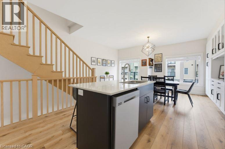 Open-concept kitchen and dining area featuring light wood-finish flooring, a contemporary kitchen island with a white countertop and integrated sink, a stainless steel dishwasher, and built-in white c - 16 Raspberry Lane, Hamilton, ON - Indoor