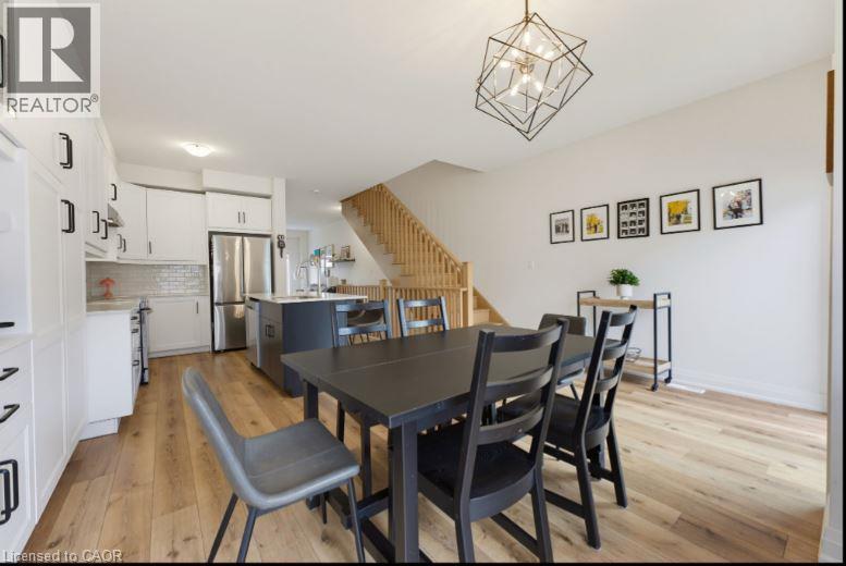 Open-concept living space featuring wood-finish flooring, a contemporary geometric chandelier, white cabinetry with black hardware, a tiled backsplash, and a wooden staircase - 16 Raspberry Lane, Hamilton, ON - Indoor Photo Showing Other Room