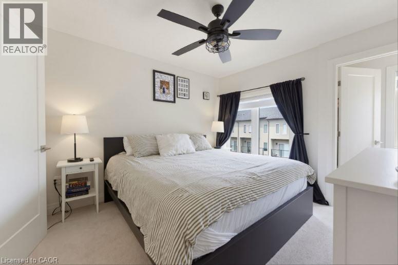 Carpeted room with a ceiling fan light fixture, white walls, and a window featuring black curtains - 16 Raspberry Lane, Hamilton, ON - Indoor Photo Showing Bedroom
