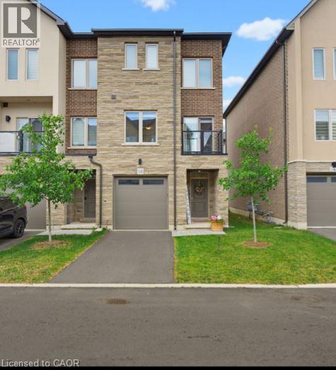 Contemporary townhouse exterior featuring a brick and stone facade, private balcony with black railings, integrated garage, and a paved driveway - 16 Raspberry Lane, Hamilton, ON - Outdoor With Facade