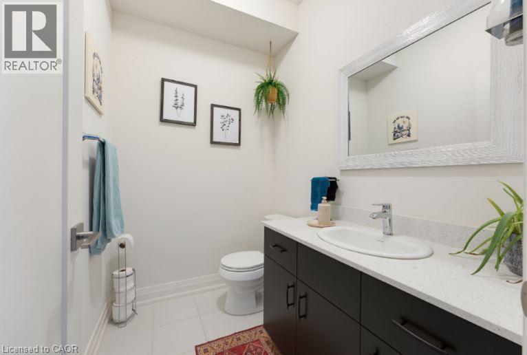 Bathroom featuring white tiled flooring, a dark wood-finish vanity with an integrated basin, a light-colored countertop, and a large framed mirror - 16 Raspberry Lane, Hamilton, ON - Indoor Photo Showing Bathroom