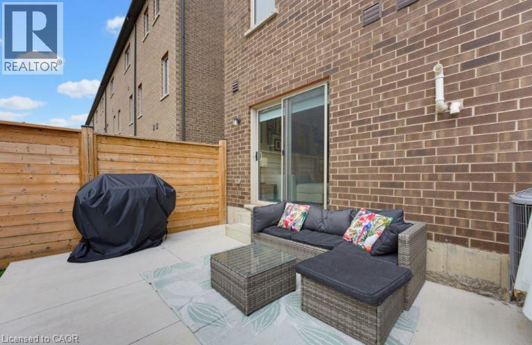Concrete patio area featuring a wooden privacy fence and brick exterior - 16 Raspberry Lane, Hamilton, ON - Outdoor With Deck Patio Veranda With Exterior