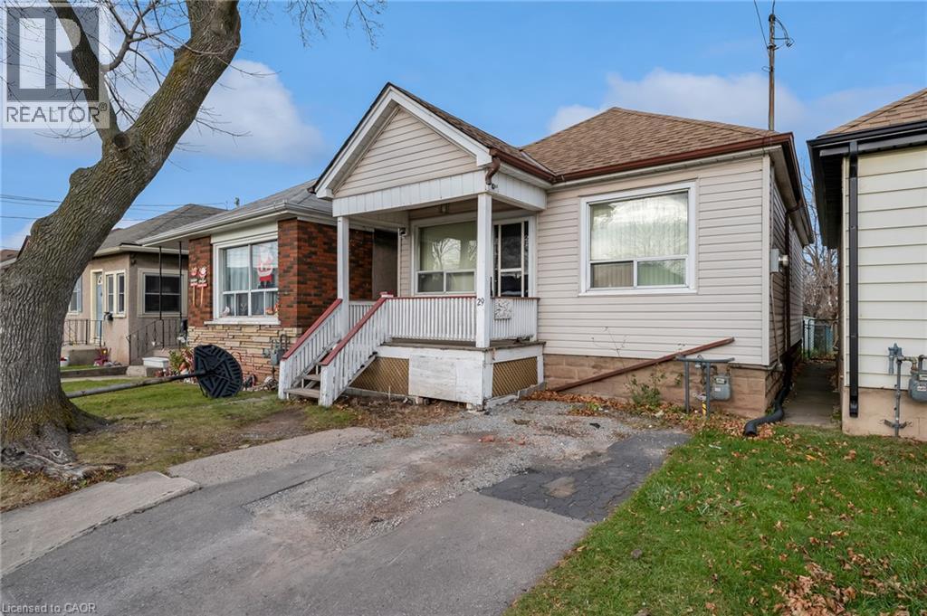 Single-story residence featuring light-colored siding, a covered porch with white railings, and a shingled roof - 29 Harrison Avenue, Hamilton, ON - Outdoor