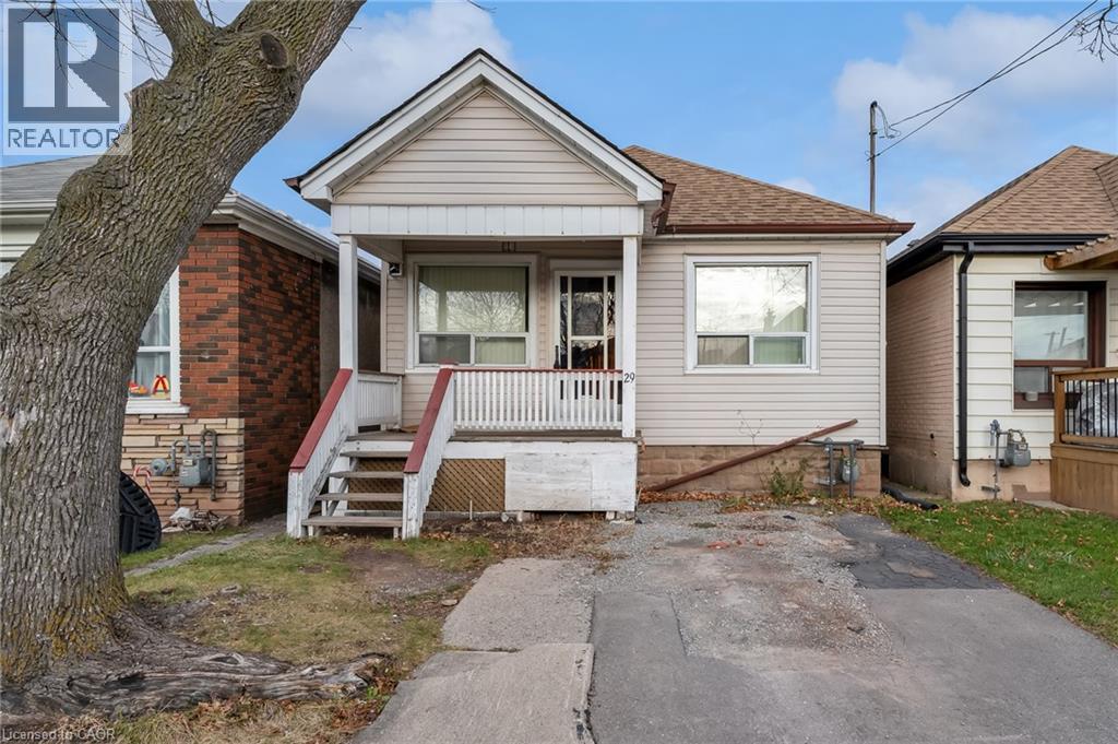 Single-story residence featuring light-colored siding and a covered front porch with white railings - 29 Harrison Avenue, Hamilton, ON - Outdoor With Deck Patio Veranda