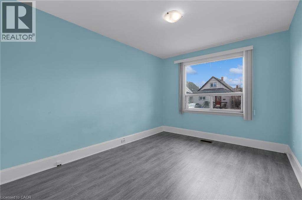 Room featuring a large window, blue painted walls, white trim, wood-finish flooring, and a ceiling-mounted light fixture - 29 Harrison Avenue, Hamilton, ON - Indoor Photo Showing Other Room