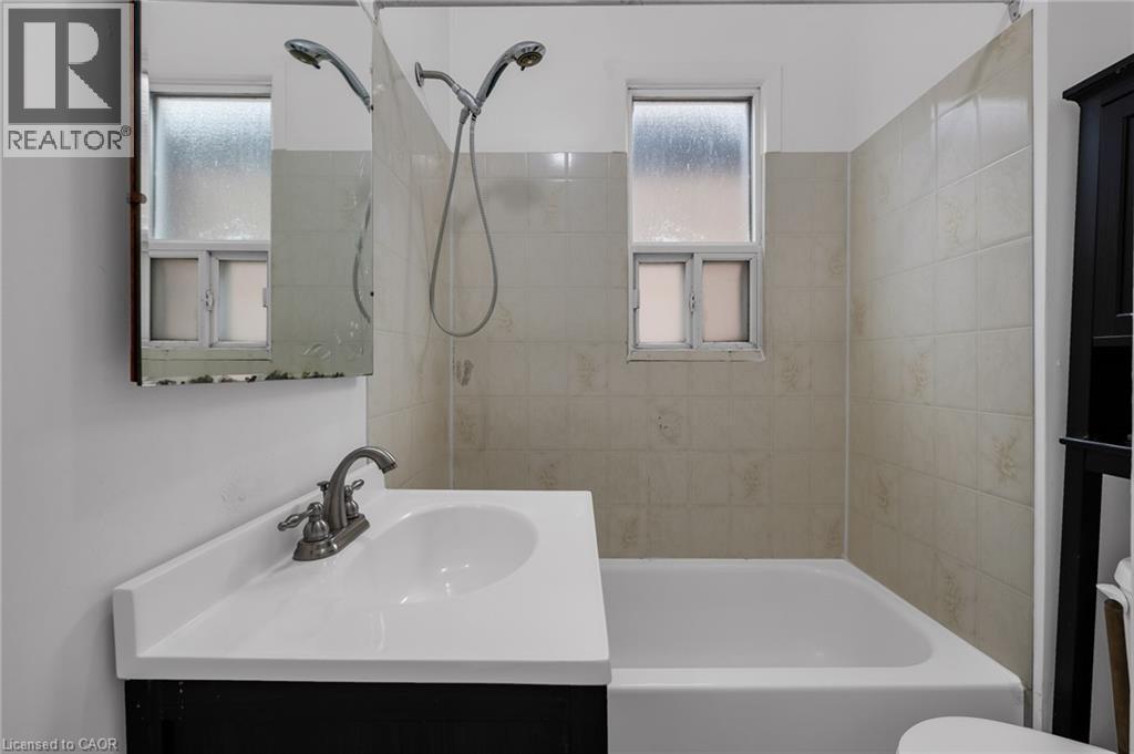 Bathroom featuring a white bathtub, a vanity with an integrated sink, a wall-mounted medicine cabinet, and a tiled shower surround - 29 Harrison Avenue, Hamilton, ON - Indoor Photo Showing Bathroom