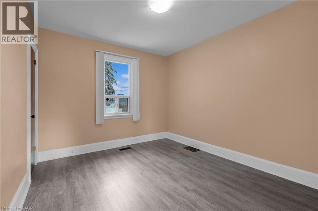 Spacious room featuring wood-finish flooring, light peach walls, and white trim - 29 Harrison Avenue, Hamilton, ON - Indoor Photo Showing Other Room