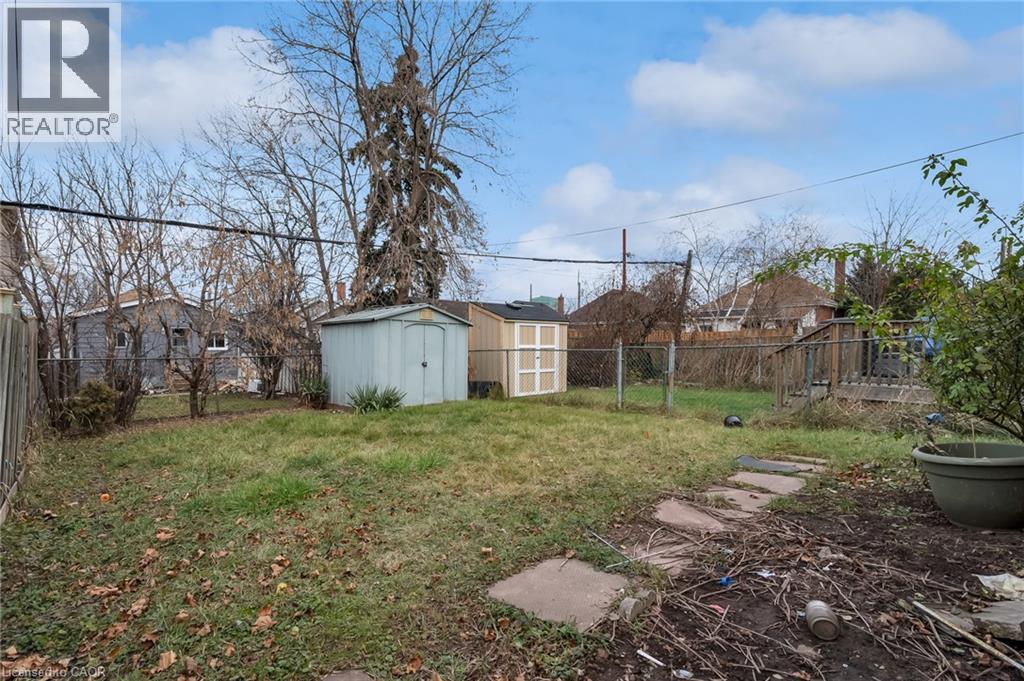 Expansive backyard featuring two storage sheds, a chain-link fence, a paved stepping stone path, and a wooden deck structure - 29 Harrison Avenue, Hamilton, ON - Outdoor