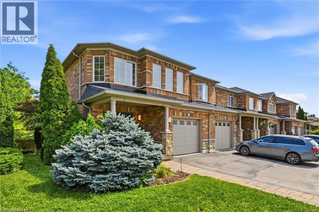 Brick exterior townhome featuring a two-car garage, stone accents, bay windows, and mature landscaping - 5628 Stella Lane, Burlington, ON - Outdoor
