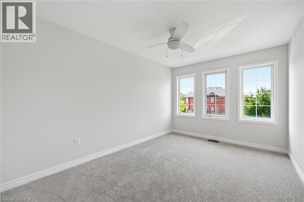 Bright room featuring three large windows, a ceiling fan, light-colored walls, and gray carpet flooring - 5628 Stella Lane, Burlington, ON - Indoor Photo Showing Other Room