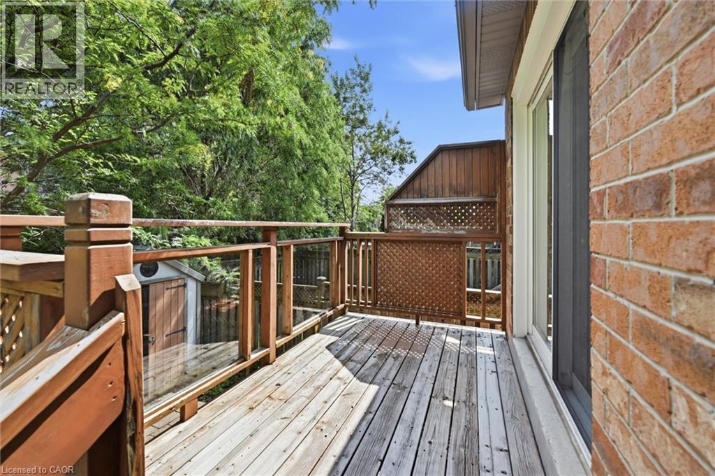 Outdoor wood deck featuring glass panel railings, a lattice privacy screen, and direct access to interior via a sliding glass door, all against a brick exterior - 5628 Stella Lane, Burlington, ON - Outdoor With Deck Patio Veranda With Exterior