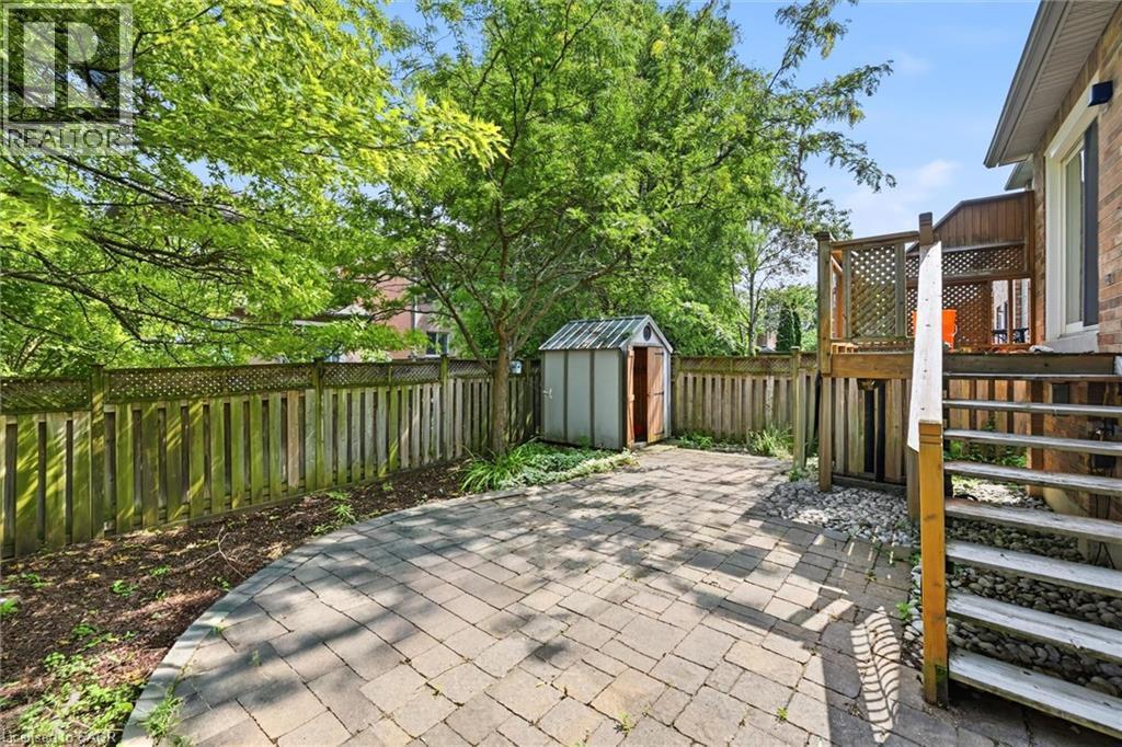 Expansive paver patio featuring a raised wood deck with lattice railing, a storage shed, and a full wooden privacy fence - 5628 Stella Lane, Burlington, ON - Outdoor