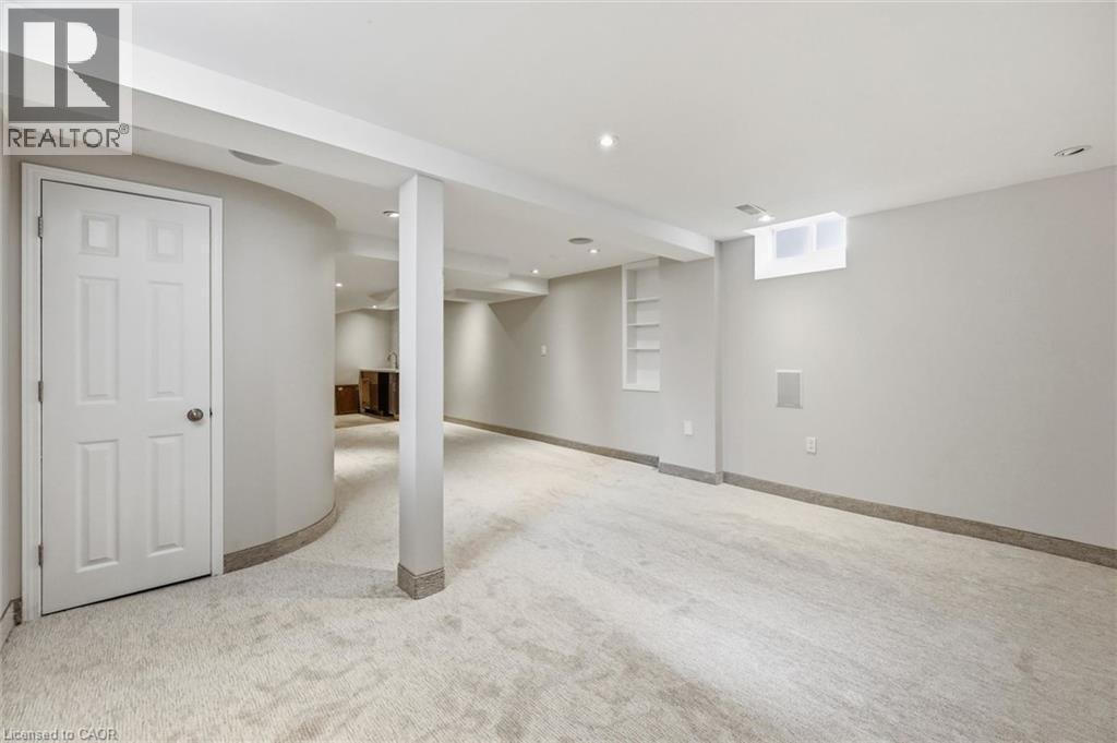 Expansive finished basement featuring recessed lighting, light-toned carpeting, a built-in shelving unit, a window, and a curved architectural wall - 5628 Stella Lane, Burlington, ON - Indoor Photo Showing Basement