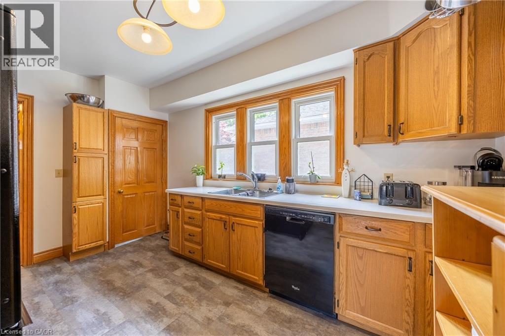 Kitchen featuring wood-finish cabinetry, solid surface countertops, and a stainless steel sink with a black dishwasher - 5 Hawthorne Avenue, Simcoe, ON - Indoor Photo Showing Kitchen With Double Sink