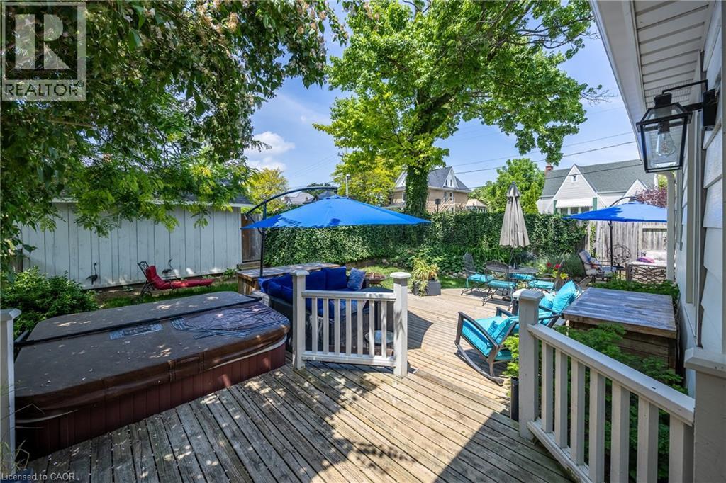 Expansive wood deck featuring a covered outdoor spa, white picket railing, and mature trees providing natural canopy - 5 Hawthorne Avenue, Simcoe, ON - Outdoor With Deck Patio Veranda