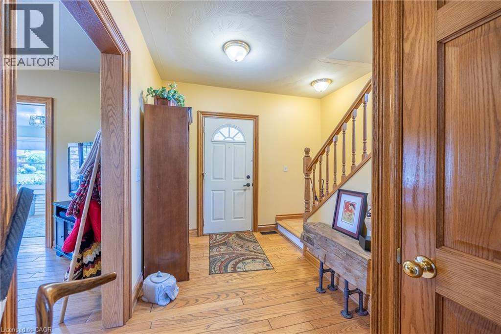 Entryway featuring wood-finish flooring, a white paneled front door with an arched glass insert, and a wooden staircase with balusters - 5 Hawthorne Avenue, Simcoe, ON - Indoor Photo Showing Other Room