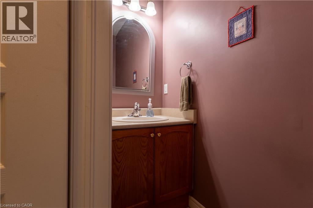 Bathroom vanity featuring a wood-finish cabinet, neutral countertop, and an arched mirror - 4066 Medland Drive, Burlington, ON - Indoor Photo Showing Bathroom