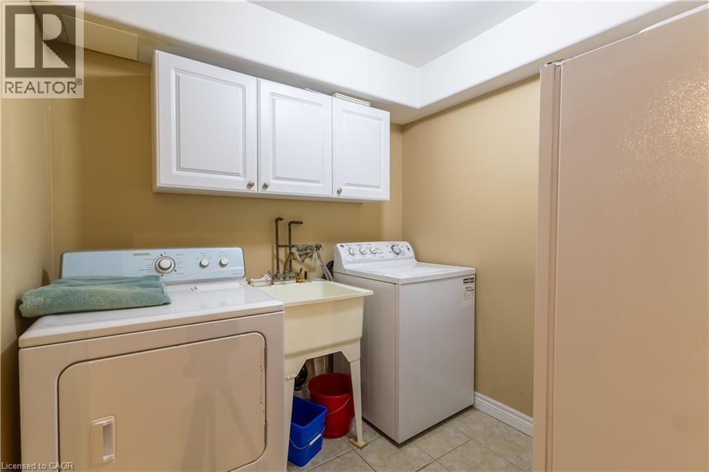 Dedicated laundry area featuring white upper cabinetry, a utility sink with dual faucets, and tiled flooring - 4066 Medland Drive, Burlington, ON - Indoor Photo Showing Laundry Room