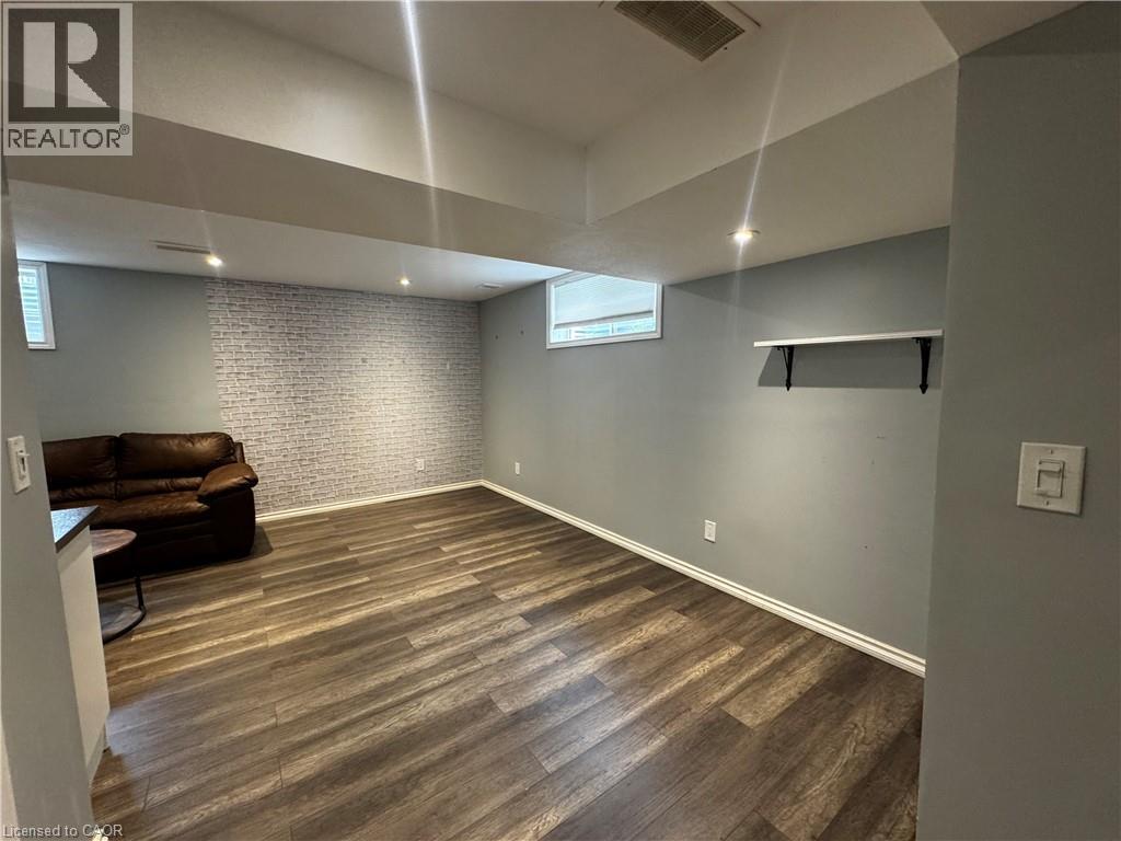 Spacious room with wood-finish flooring, recessed lighting, and a textured brick accent wall - 13 Sorrento Street, Kitchener, ON - Indoor