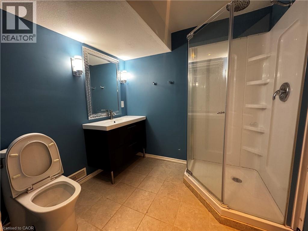 Bathroom featuring a glass-enclosed shower, freestanding vanity with integrated sink, decorative framed mirror, and two wall sconces - 13 Sorrento Street, Kitchener, ON - Indoor Photo Showing Bathroom