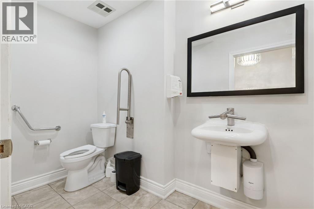 Wheelchair Accessible Bathroom, wall-mounted sink with integrated faucet, contemporary wall mirror, white toilet, and grab bars. - 189 Hughson Street, Hamilton, ON