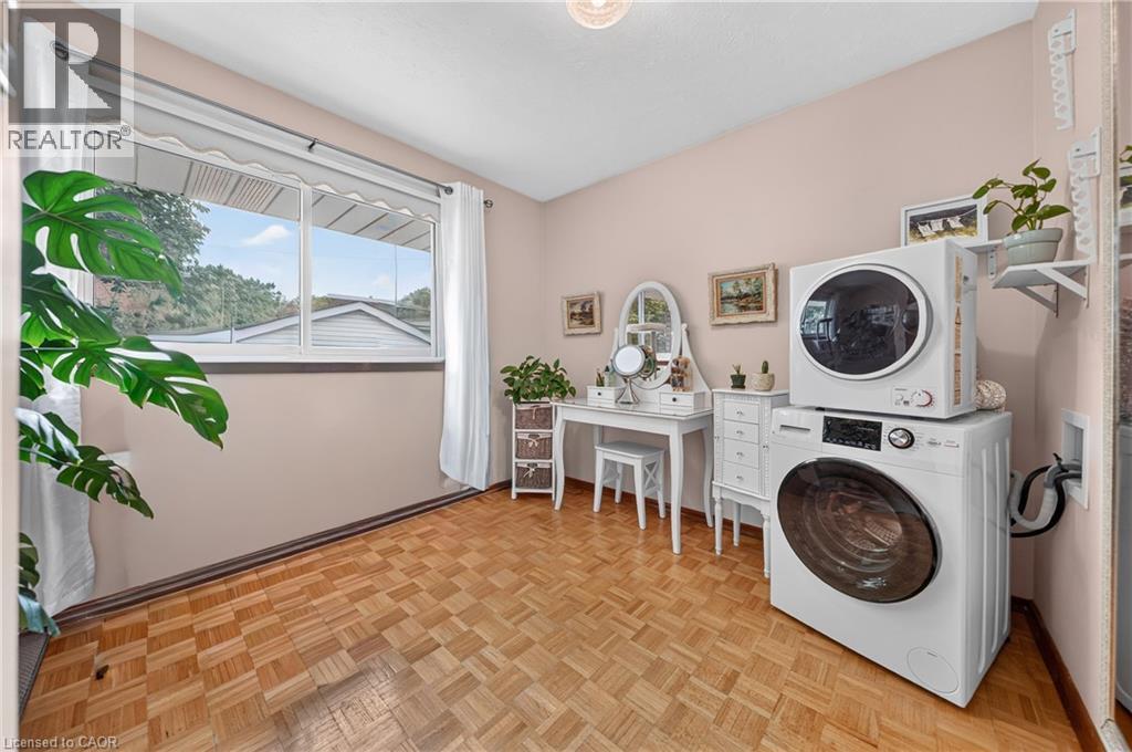 Room featuring parquet wood-finish flooring, a large window with white trim, and a built-in laundry appliance stack - 111 Kimberly Crescent, Kitchener, ON - Indoor Photo Showing Laundry Room